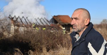 Muškarac stoji ispred izgorjele kuće s oteglinama u pozadini