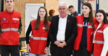 Grupa ljudi u crvenimalth uniformama i službenik poziraju na akciji darivanja krvi