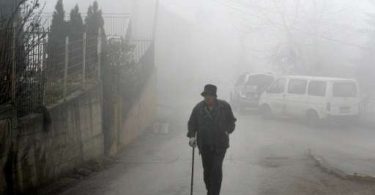Osoba hoda kroz gustu maglu na ulici s automobilom u pozadini