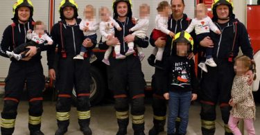 Група vatrogасаца у униформама са осморо новорођене деце позирана за фотографију