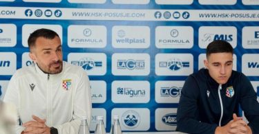 Dva člana HŠK Posušja na konferenciji za medije; čovjek u bijeloj jakni govori u mikrofon