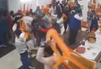 Grupa ljudi u tradicijskim saffron odjećama u fizičkom sukobu unutar zatvorenog prostora
