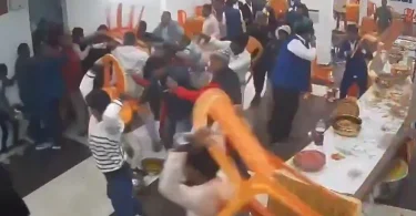 Grupa ljudi u tradicijskim saffron odjećama u fizičkom sukobu unutar zatvorenog prostora