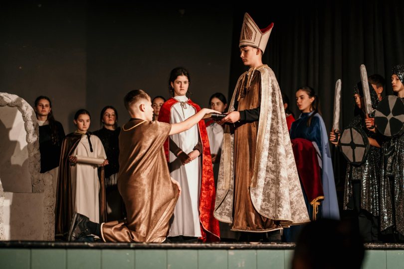 Scena iz predstave Krunidba s glumcima u historijskim kostimima, kralj sjedi na prijestolju okružen svojom povorkom