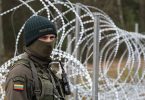 Vojnik u uniformi i maski stoji pored bodljikave žice na granici