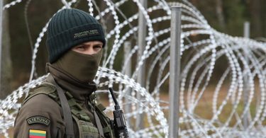 Vojnik u uniformi i maski stoji pored bodljikave žice na granici