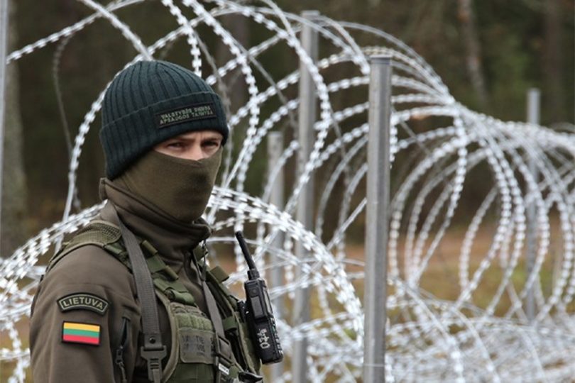 Vojnik u uniformi i maski stoji pored bodljikave žice na granici