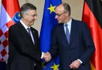 Dvojica muškaraca u odjelima rukuju se ispred hrvatskog i njemačkog zastava te EU zastave