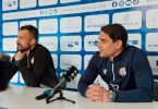 Dvojica muškaraca sjedne za stolom s mikrofonom tijekom press konferencije