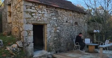 Kamena kuća s drvenim vratima, obnovljena s bijelim namještajem ispred