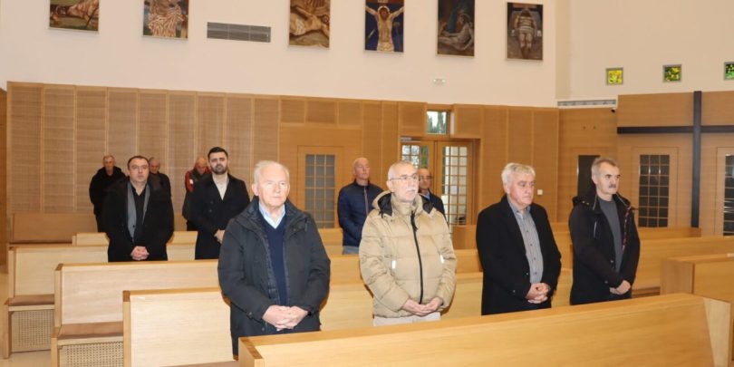 Grupa muškaraca u formalnoj odjeći stoji u crkvi tijekom vjerske ceremonije