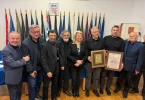 Grupa muškaraca u formalnoj odjeći s plaketom i признањем na ceremoniji