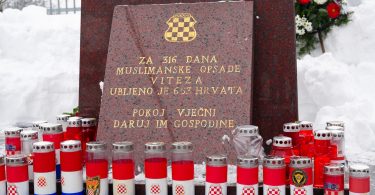 Spomen-ploča od crvenog mramora s hrvatskom šahovnicom i svijećama te crno-bijelim zastavama