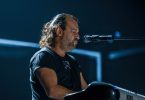 Muzičar pjeva pri mikrofonu tijekom live koncerta sa scenskom rasvjetom