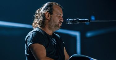 Muzičar pjeva pri mikrofonu tijekom live koncerta sa scenskom rasvjetom