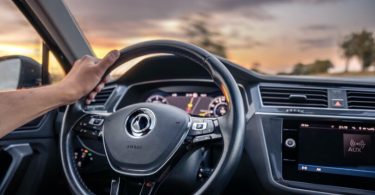 Unutrašnjost automobila s vožnjom pri zalasku sunca, ruka na volanu