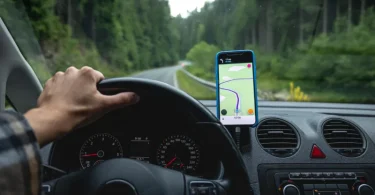 Vozač drži volan jednom rukom dok gleda pametni telefon sa Google Maps navigacijom