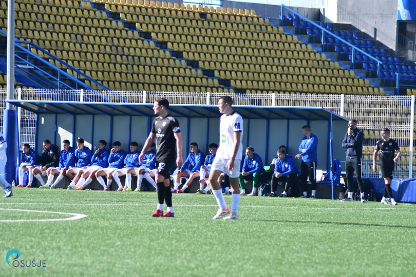 Fudbalski meč između dva tima na stadionu sa gledalištem u pozadini