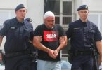 Muž u crvenoj majici između dva policajca tokom hvatanja