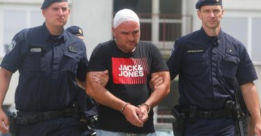 Muž u crvenoj majici između dva policajca tokom hvatanja