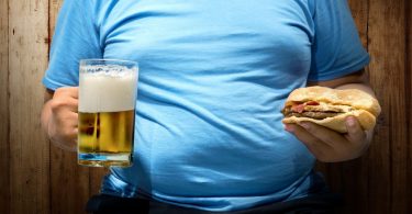 Muškarac u plavoj majici drži pivo i sendvič
