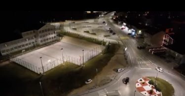 Noćni pogled na osvetljeno sportsko igralište s reflektorima i parkiralištem