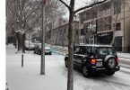 Crni automobil parkirab na snježnoj ulici s голих stabala i gradskih zgrada