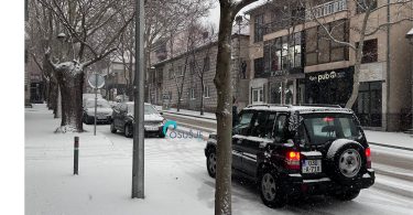 Crni automobil parkirab na snježnoj ulici s голих stabala i gradskih zgrada