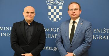 Dva muškarca u poslovnom odijelu pred zidnom s grbom i logotipom ministarstva