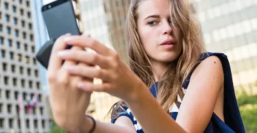 Mlada žena fotografira sebe pametnim telefonom na javnoj lokaciji
