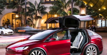 Crvena Tesla Model X s karakterističnim otvarajućim vratima parkirana ispred luksuzne zgrade