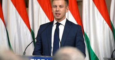 Muškarac u tamnom odijelu pri mikrofonu s natpisom TISZA na pozadini mađarskih zastava