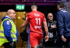 Igrač u crvenom dresu broj 11 odlazi sa stadiona praćen lekarom i stručnjacima