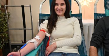 Žena u bijeloj majici sjeđi na stolici tijekom doniranja krvi
