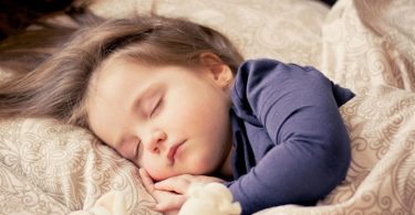 Malo dijete mirno spava u krevetu s plavo-bijelom pidžamom
