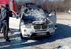 Bijeli BMW s otvorenim haубom u plamenu, vatrogasci gase požar