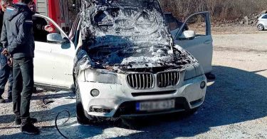 Bijeli BMW s otvorenim haубom u plamenu, vatrogasci gase požar