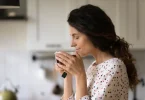 Žena s dugom crnom kosom pije toplu šalicu čaja iz bele šolje u kuhnji