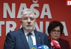 Muž u plavom odijelu i naočalama napress konferenciji uz crvenu pozadinu