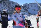 Skijašica u skijaški opremi s italijanskom zastavom na leđima, s gorama u pozadini
