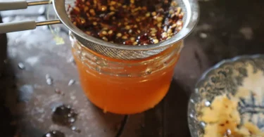 Staklena teglica s narančastim hot honey medom i crvenim ljutim paprima.