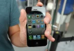 Ruka koja drži iPhone 4 sa prikazanim home screenom i aplikacijama