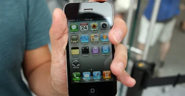 Ruka koja drži iPhone 4 sa prikazanim home screenom i aplikacijama