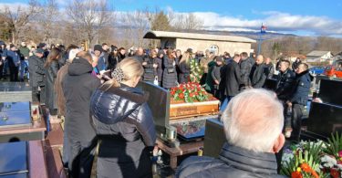 Okupljeni građani na sprovodu s cvijećem i vjerskim simbolima
