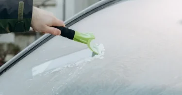 Osoba briše led s vjetrobrana automobila plastičnom skropalicom