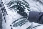 Ruka u rukavici skida led sa vjetrobranskog stakla automobila