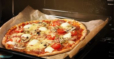 Свежа пица са моцарелом и томатима на папиру за печење у пећници