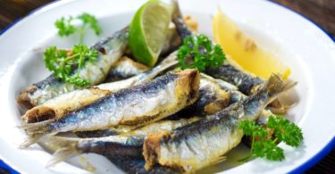 Pečene sardine na bijeloj tanjuri s limunskom rezinom i peršilom