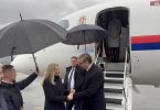 Zvanična osoba s dužnosnicima izlazi iz aviona na kišnom vremenu s kišobranom