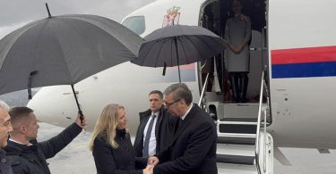 Zvanična osoba s dužnosnicima izlazi iz aviona na kišnom vremenu s kišobranom